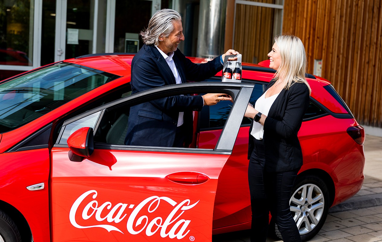 Zwei Mitarbeiter:innen vor einem roten Coke Auto