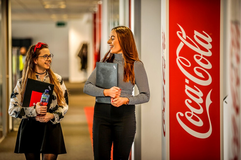 Two women with laptops in hand in a corridor in the office