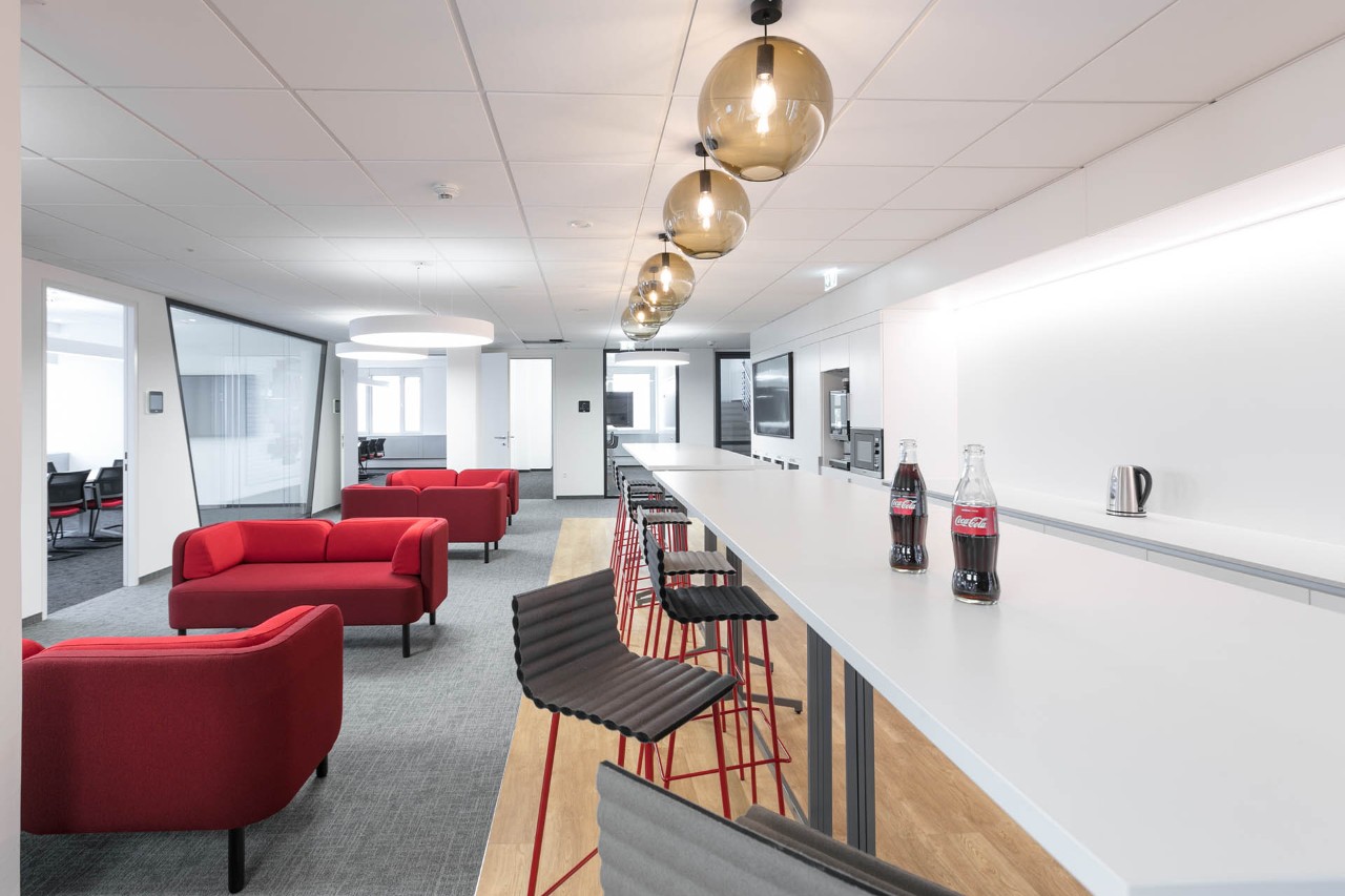 Open office area with three red sofas and two high bar tables